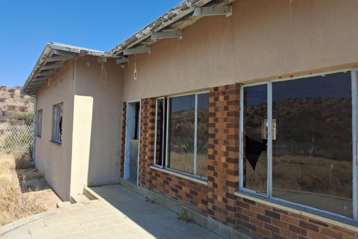 Rear exterior view of a residential property showing a paved patio, brick facade, and damaged window frames requiring maintenance and repair.