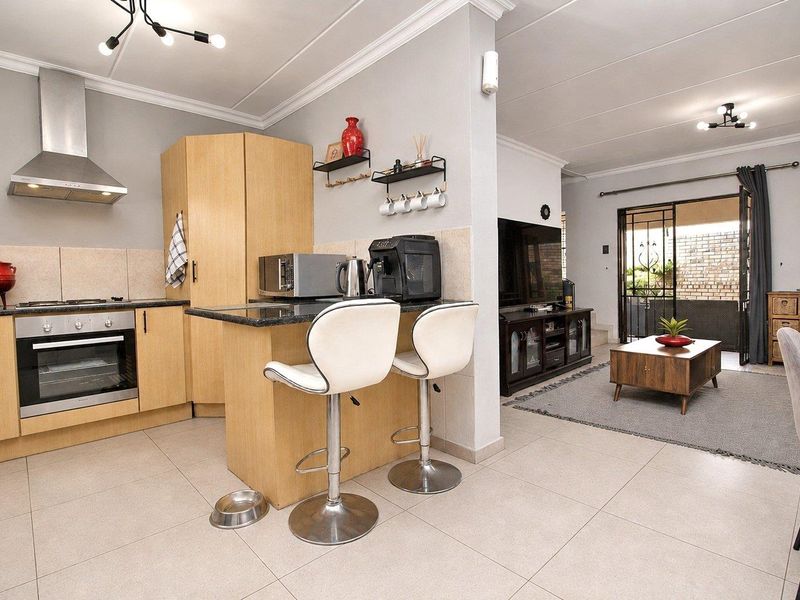 Open-plan kitchen and living area featuring light wood cabinetry, granite countertops, stainless steel appliances, and tiled flooring with access to an outdoor patio.