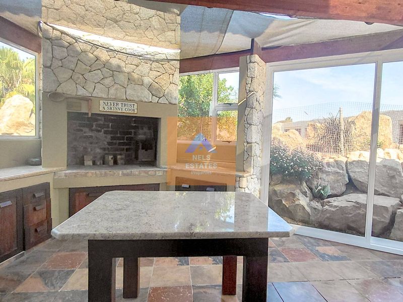 Covered patio area featuring a built-in stone braai, granite prep surfaces, and large sliding glass doors opening to a landscaped garden.