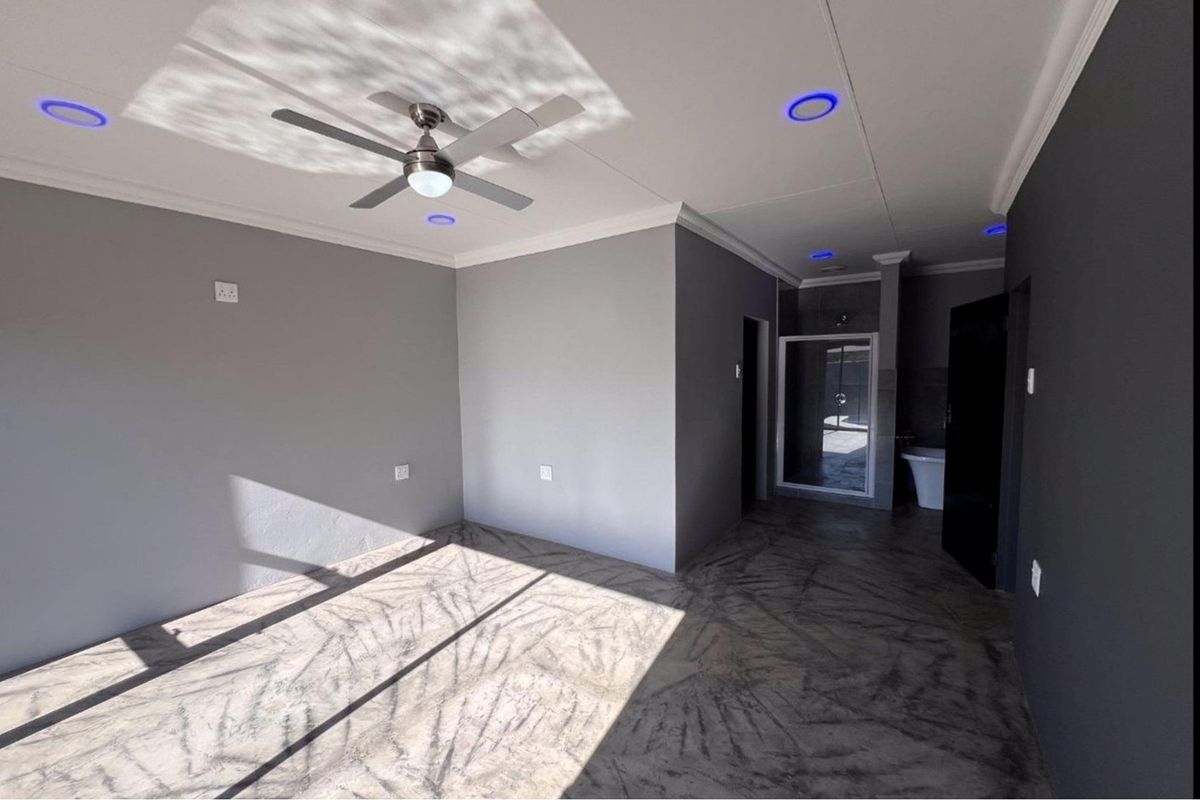 Spacious bedroom featuring polished concrete floors, a ceiling fan, recessed lighting, and an open-plan en-suite bathroom with a shower and freestanding tub.