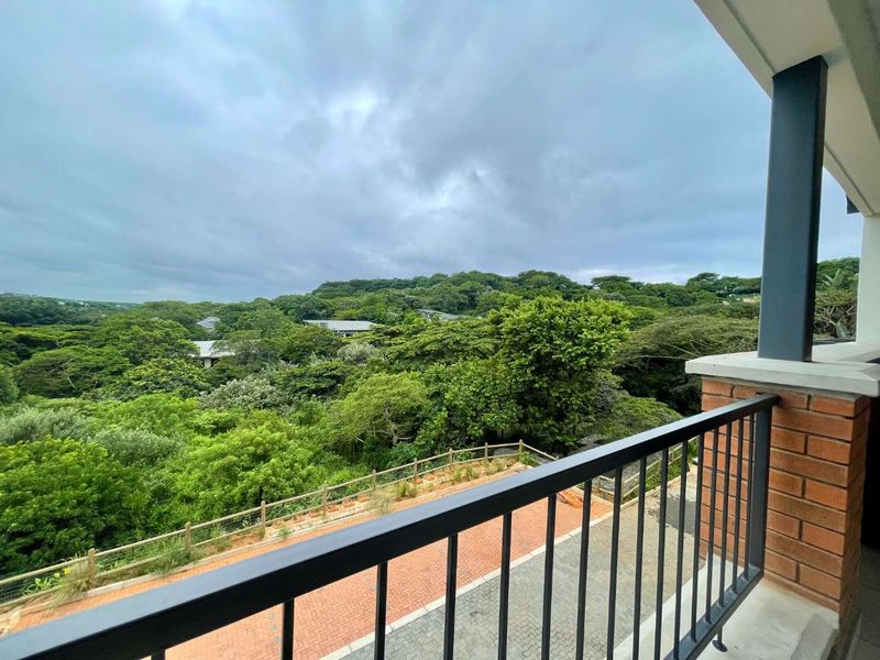 A covered balcony featuring a metal balustrade and brick pillar, offering an elevated view over the surrounding lush green landscape.