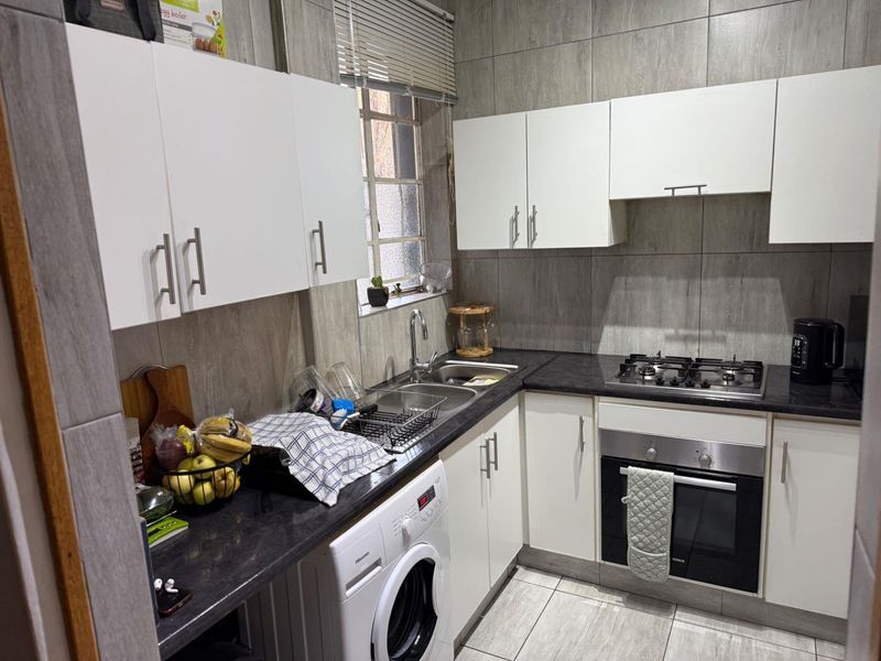 A functional kitchen featuring white cabinetry, dark countertops, a gas hob, built-in oven, and tiled finishes throughout.