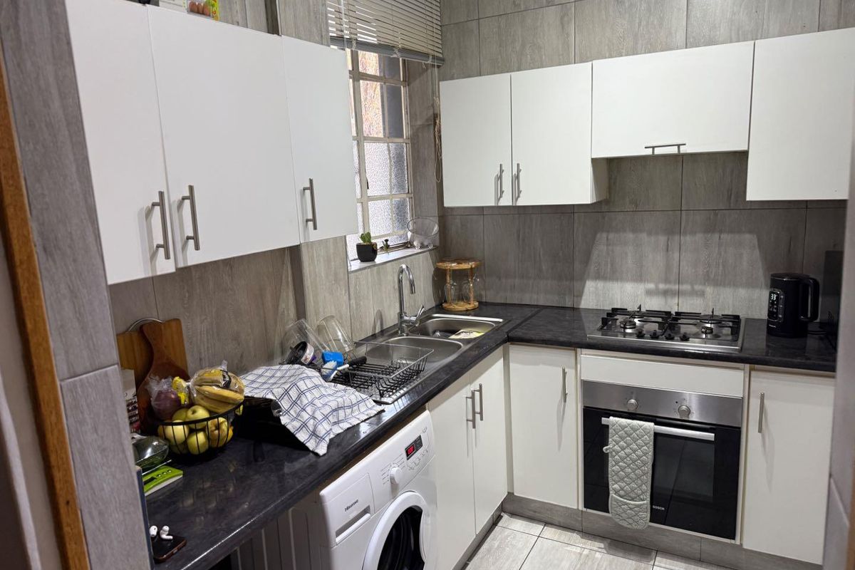 A functional kitchen featuring white cabinetry, dark countertops, a gas hob, built-in oven, and tiled finishes throughout.