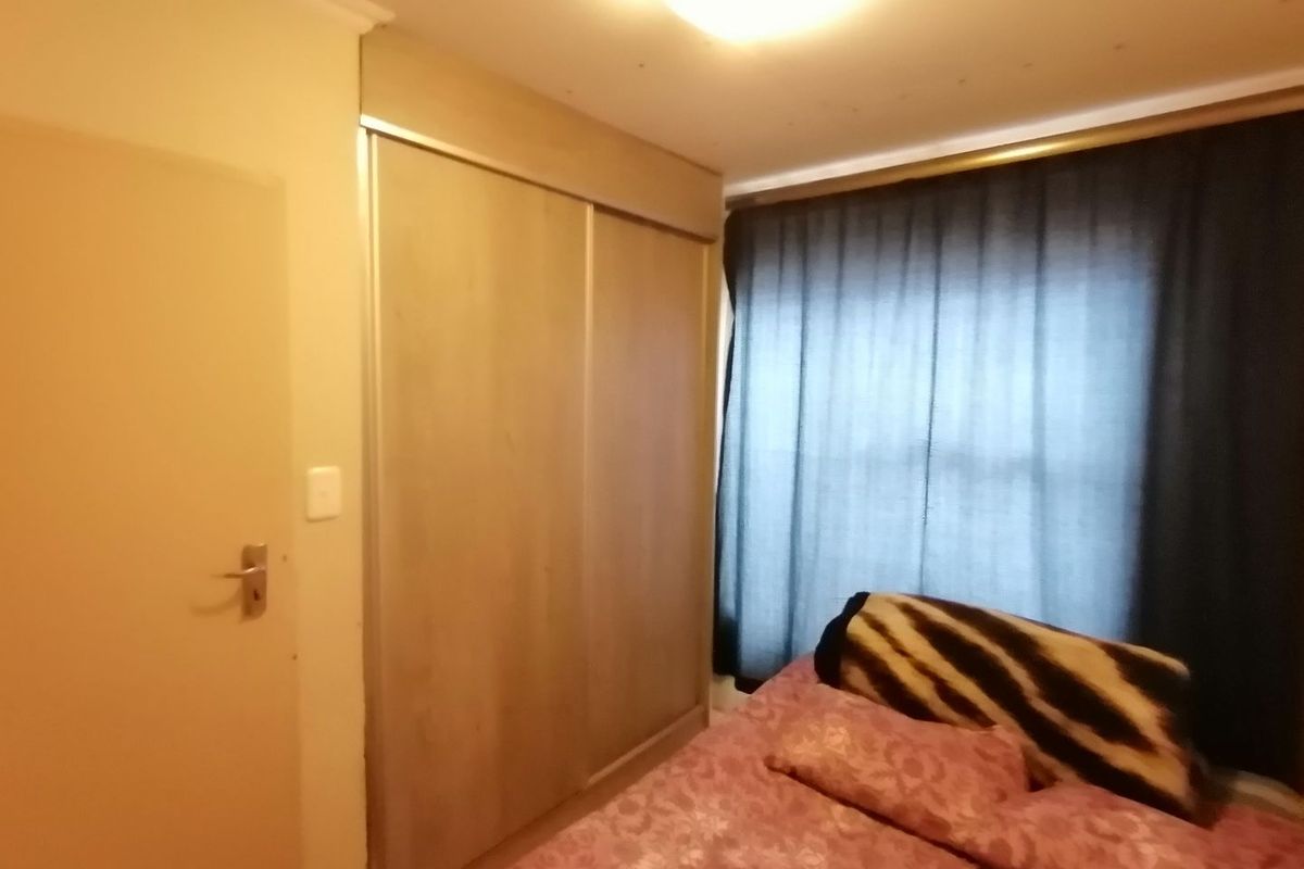 A bedroom featuring built-in sliding door cupboards and a window with dark curtains.