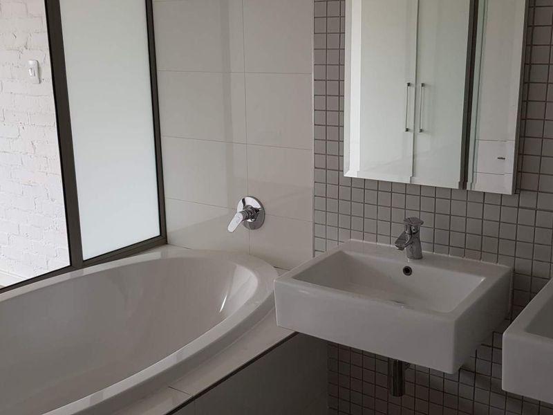 Modern bathroom featuring a built-in bathtub, dual wall-mounted vanity basins with chrome fixtures, and a mirrored medicine cabinet with tiled splashback.