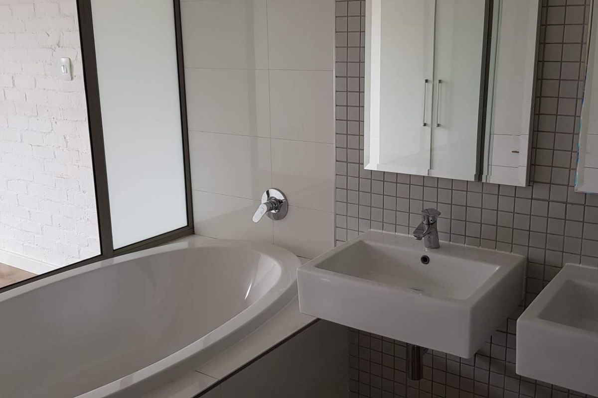 Modern bathroom featuring a built-in bathtub, dual wall-mounted vanity basins with chrome fixtures, and a mirrored medicine cabinet with tiled splashback.