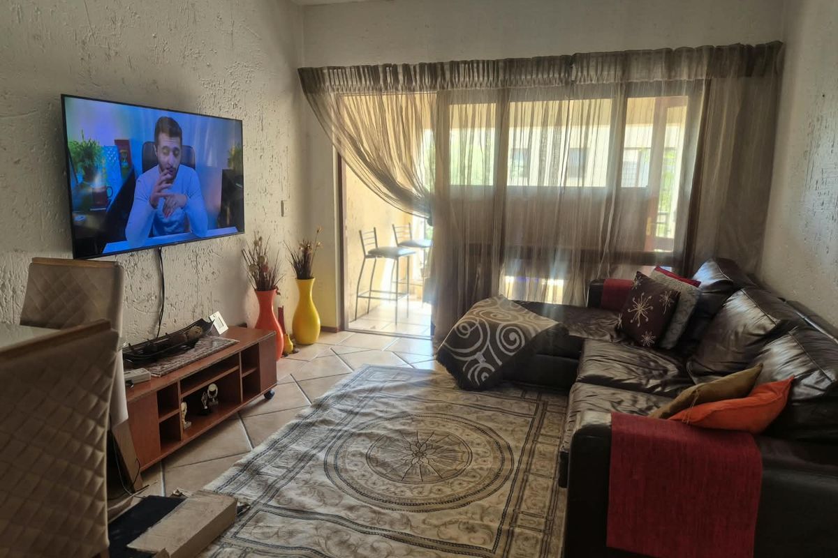 A living room featuring ceramic floor tiles and a sliding glass door leading to a balcony, with textured wall finishes.
