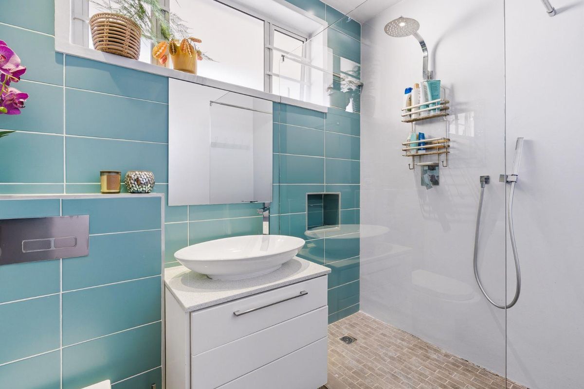 Modern bathroom featuring a vessel sink on a stone vanity, a walk-in shower with a rain head, and vibrant blue wall tiling.