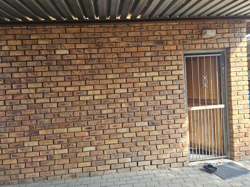 A rear exterior view featuring a face brick wall, corrugated metal roofing, and a secure metal gate leading into the property.
