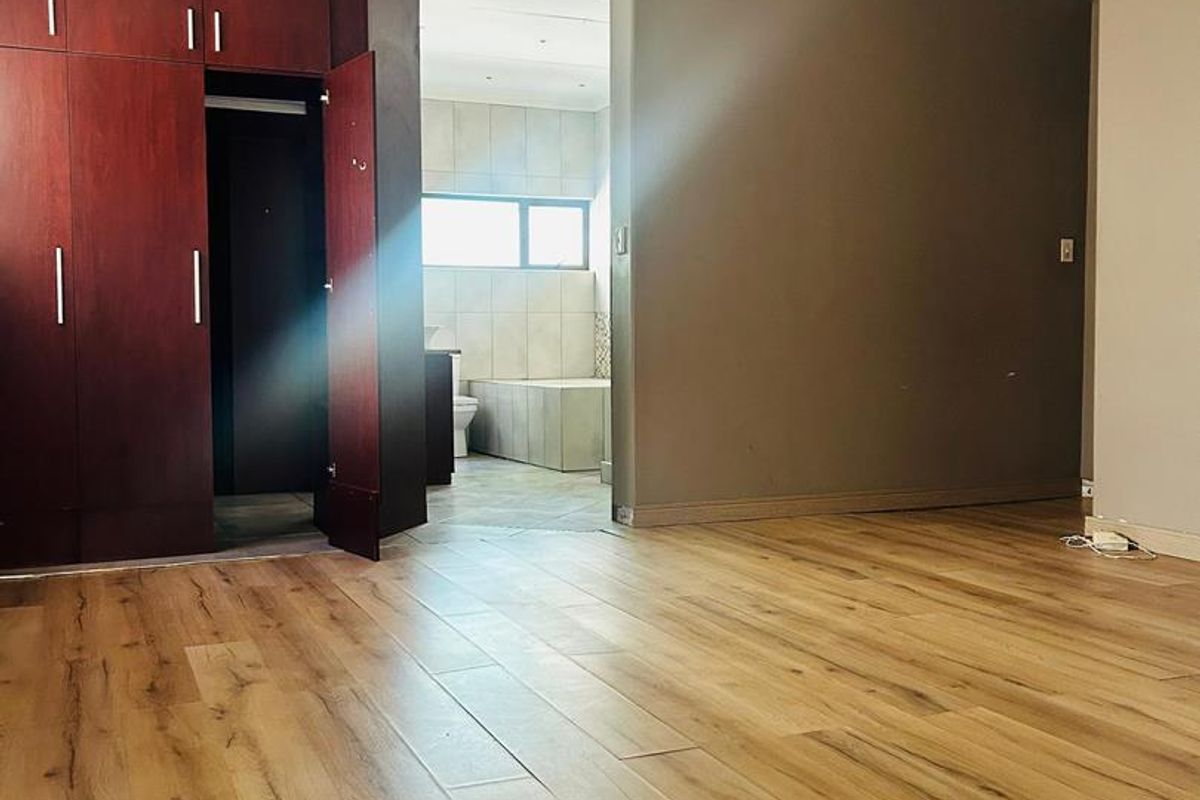 Spacious bedroom featuring wood-look laminate flooring, built-in dark wood cabinetry, and an open-plan transition into an en-suite bathroom area.