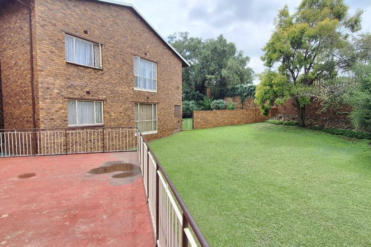 A view of the rear exterior featuring a paved patio area with metal railings overlooking a private lawn and brick boundary wall.