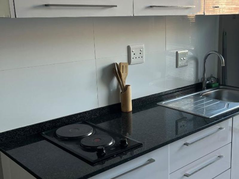 Modern kitchen featuring white gloss cabinetry, black granite countertops, an integrated electric hob, and a stainless steel sink with a tiled splashback.