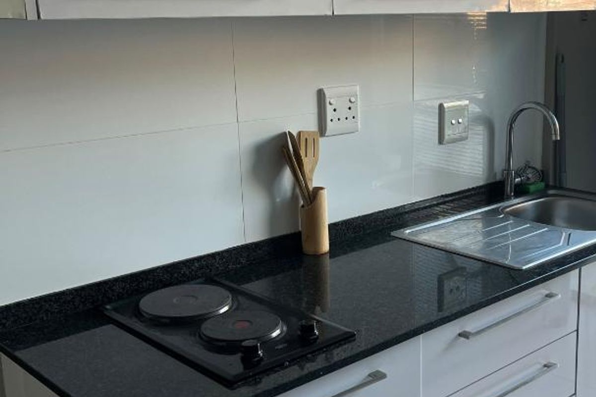 Modern kitchen featuring white gloss cabinetry, black granite countertops, an integrated electric hob, and a stainless steel sink with a tiled splashback.