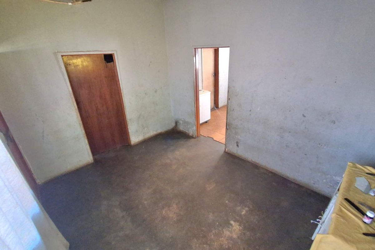 An empty bedroom in need of significant renovation, featuring exposed ceiling beams, worn wall finishes, and unfinished flooring.