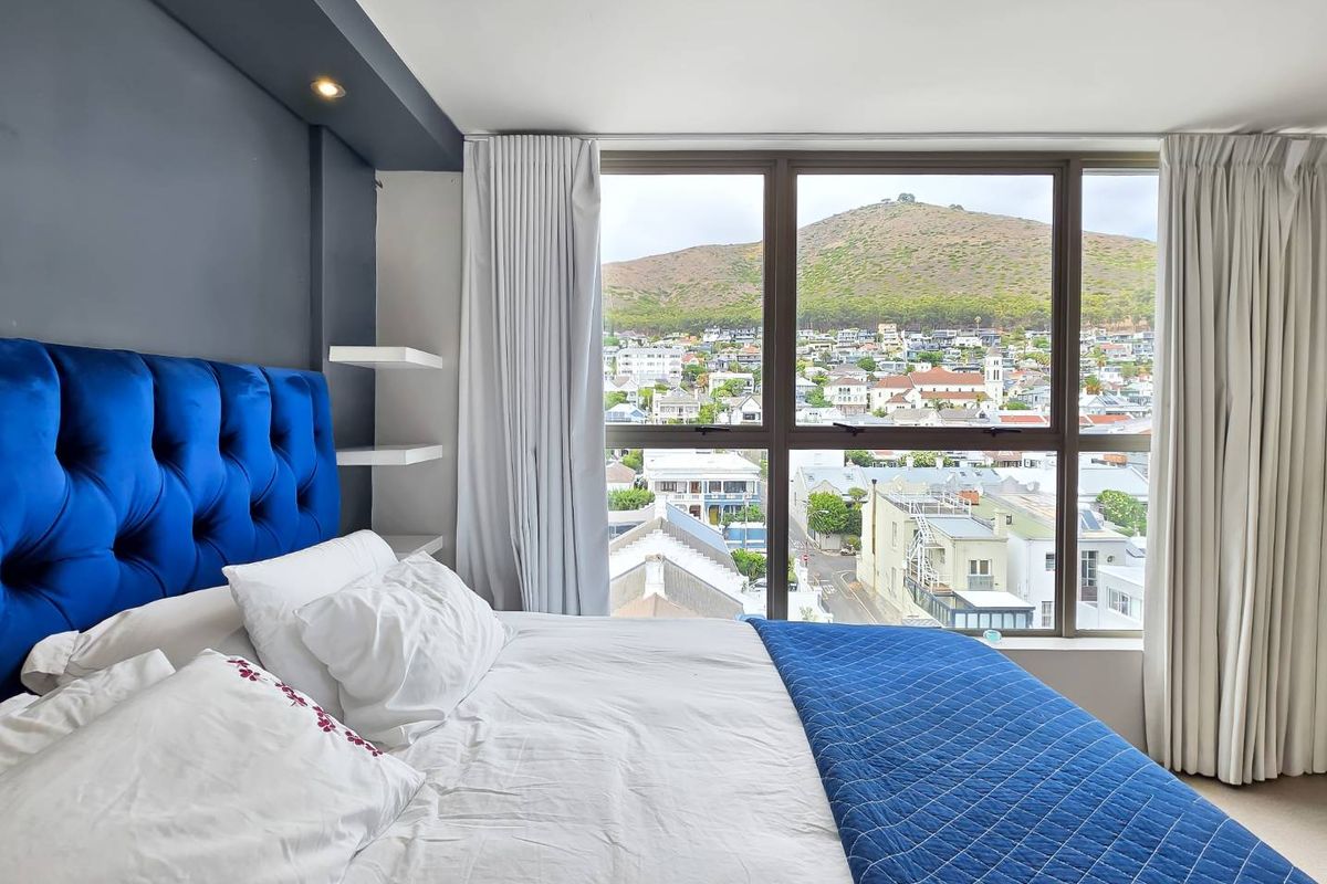A well-maintained bedroom featuring large windows that offer expansive views of the surrounding neighborhood and mountain landscape.