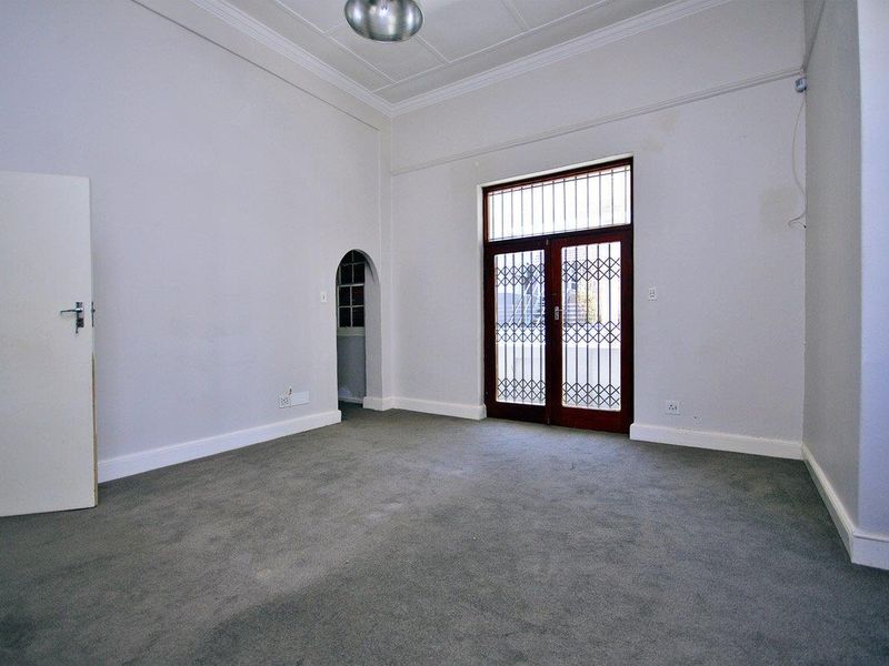 An empty living room featuring carpet flooring, a decorative coved ceiling, and a secure double door entrance with an adjacent arched doorway.