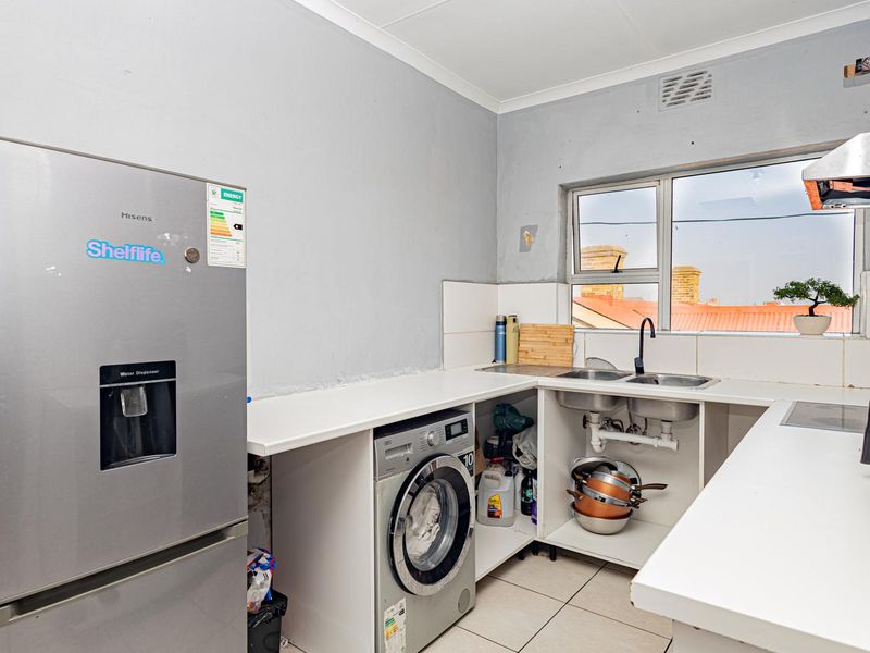Compact kitchen featuring a double sink, tiled countertops, and built-in extractor fan, requiring some cosmetic updates to cabinetry and finishes.