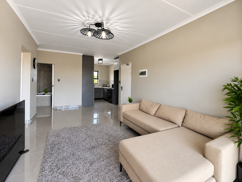 A bright open-plan living area featuring polished tiled floors, neutral walls, and a seamless transition into the adjacent kitchen space.