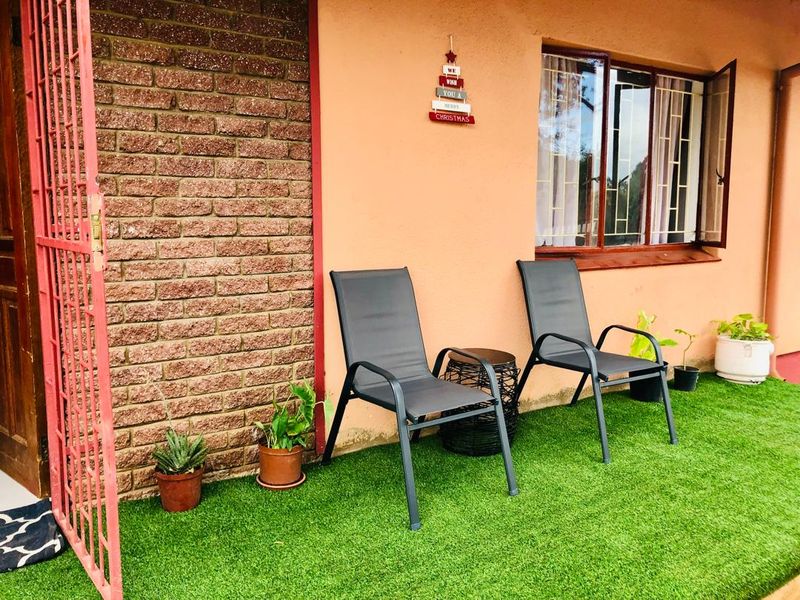A covered patio area featuring a brick feature wall, aluminium window frames, and artificial grass flooring, providing a functional outdoor space.