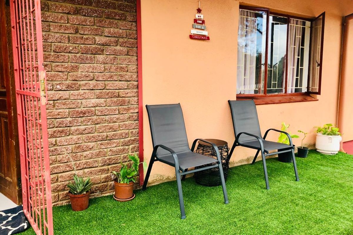 A covered patio area featuring a brick feature wall, aluminium window frames, and artificial grass flooring, providing a functional outdoor space.