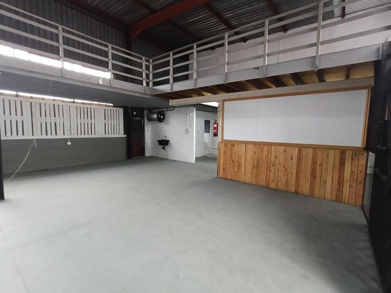 Spacious industrial utility area featuring a mezzanine level, concrete flooring, exposed steel structure, and a wall-mounted basin.