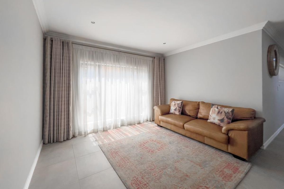 A bright and neutral living room featuring large floor-to-ceiling curtains, recessed downlighting, and modern tiled flooring.