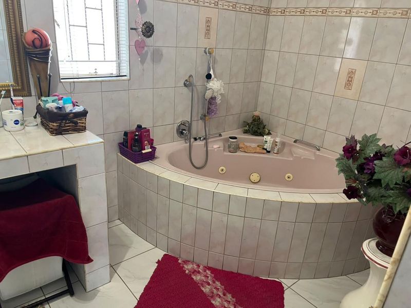 A bathroom featuring a corner bathtub with integrated jets, tiled wall finishes, and a built-in vanity area with a window.