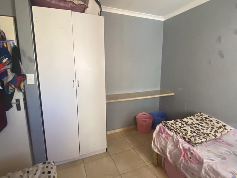 A bedroom featuring tiled flooring, a built-in wardrobe, and a fixed wall shelf, requiring minor cosmetic wall repairs.