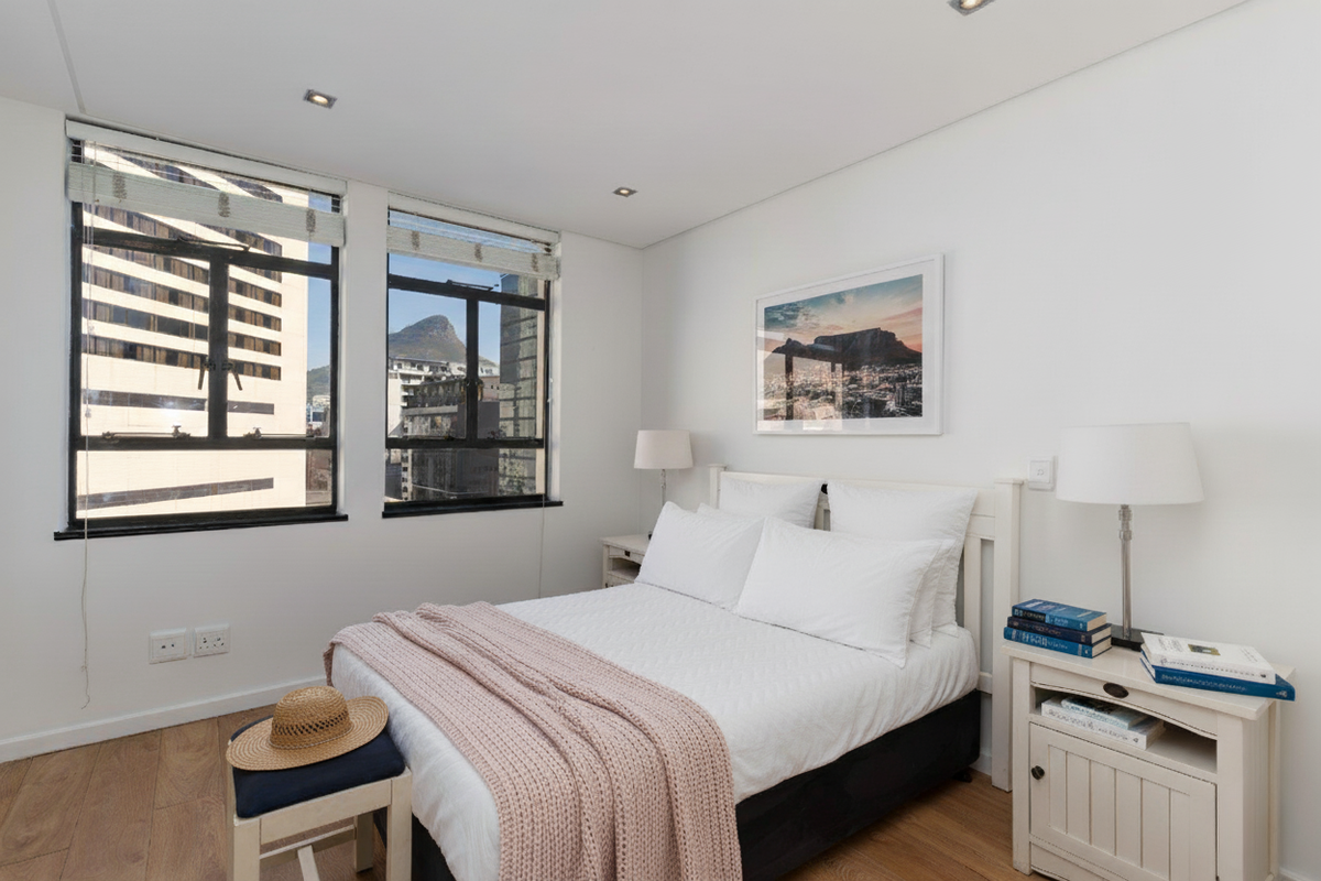 A bright and well-maintained bedroom featuring timber flooring, recessed downlighting, and large casement windows offering urban views.