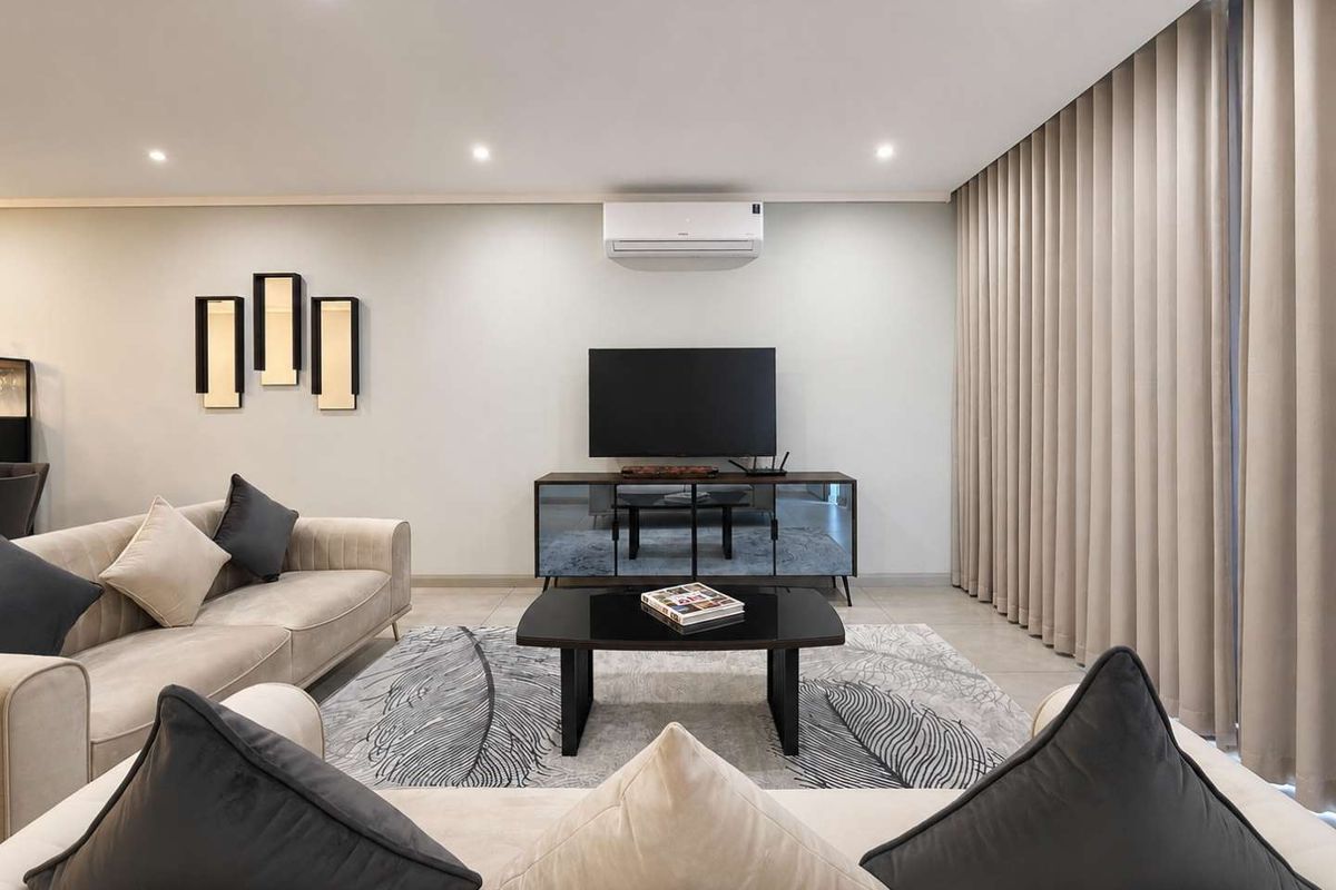 A modern, well-maintained living room featuring recessed lighting, a wall-mounted air conditioning unit, and floor-to-ceiling curtains.