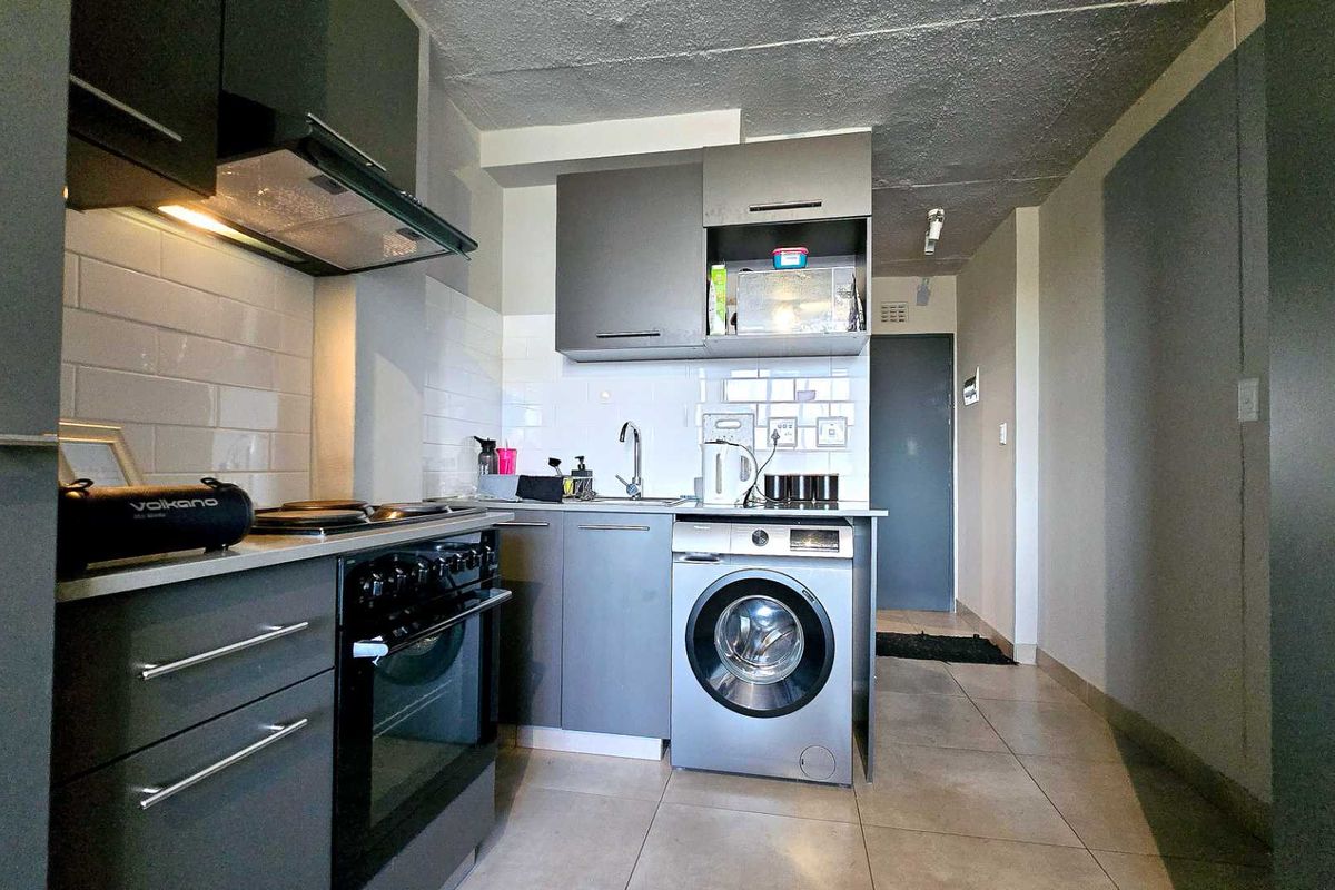 A compact, modern kitchen featuring grey cabinetry, subway tile backsplash, stainless steel appliances, and tiled flooring, providing a functional and efficient cooking space.