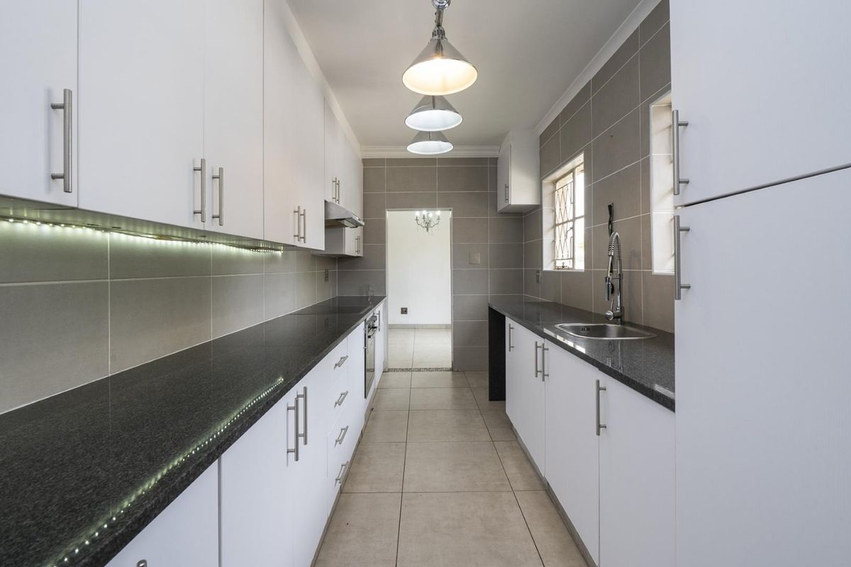 Modern galley-style kitchen featuring white cabinetry, dark granite countertops, tiled backsplash, integrated oven, and stainless steel sink.