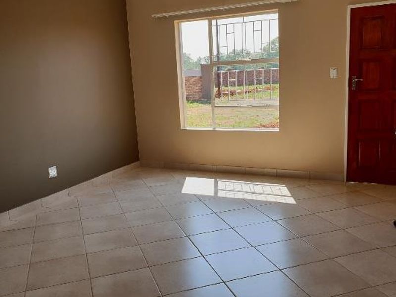 An empty living room featuring neutral-toned walls, tiled flooring, and a window fitted with security bars.
