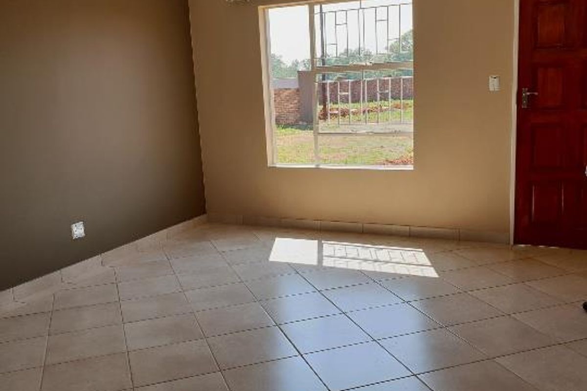 An empty living room featuring neutral-toned walls, tiled flooring, and a window fitted with security bars.
