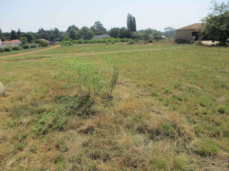A wide-angle view of a vacant residential plot featuring open grassland and surrounding neighborhood structures.