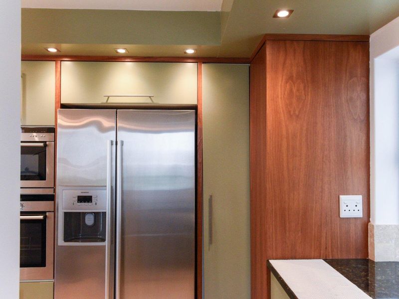 Modern kitchen featuring integrated stainless steel appliances, custom wood-toned cabinetry, granite countertops, and recessed lighting.