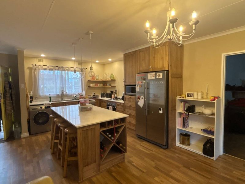 Spacious kitchen featuring a central island with stone countertop, ample wooden cabinetry, integrated appliances, and warm laminate flooring.