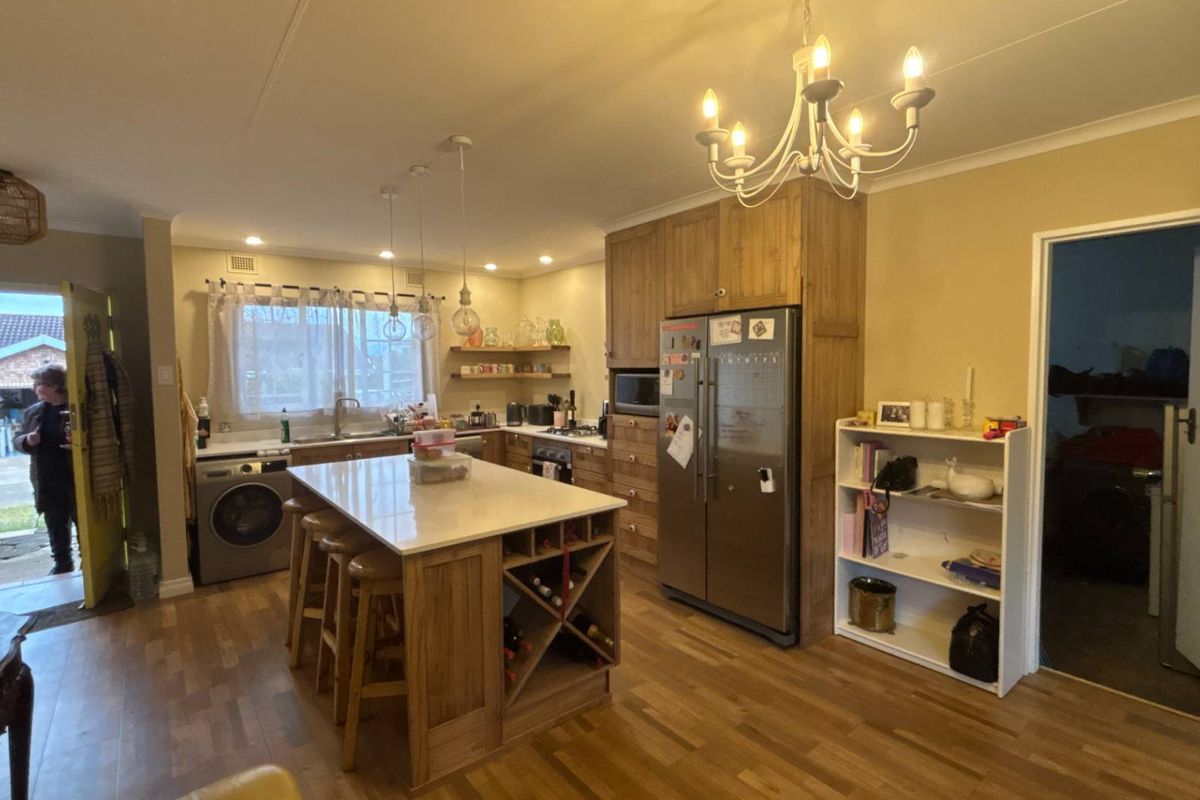 Spacious kitchen featuring a central island with stone countertop, ample wooden cabinetry, integrated appliances, and warm laminate flooring.