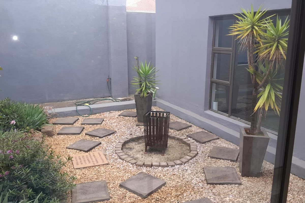 A low-maintenance rear courtyard featuring gravel landscaping, stone pavers, and a central fire pit area enclosed by high boundary walls.