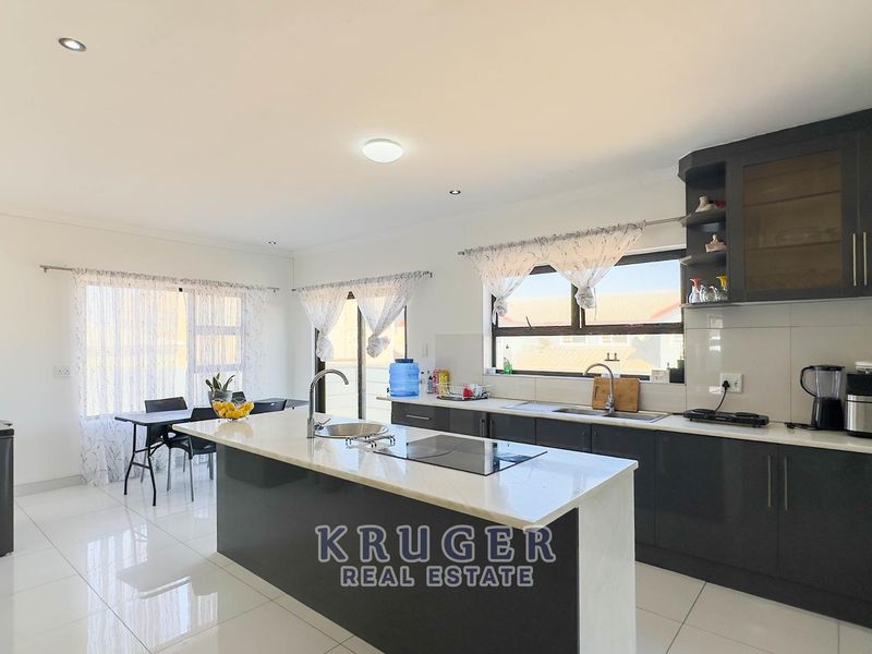Modern open-plan kitchen featuring a central island, stone countertops, dark cabinetry, and sleek tiled flooring, seamlessly flowing into the dining area.
