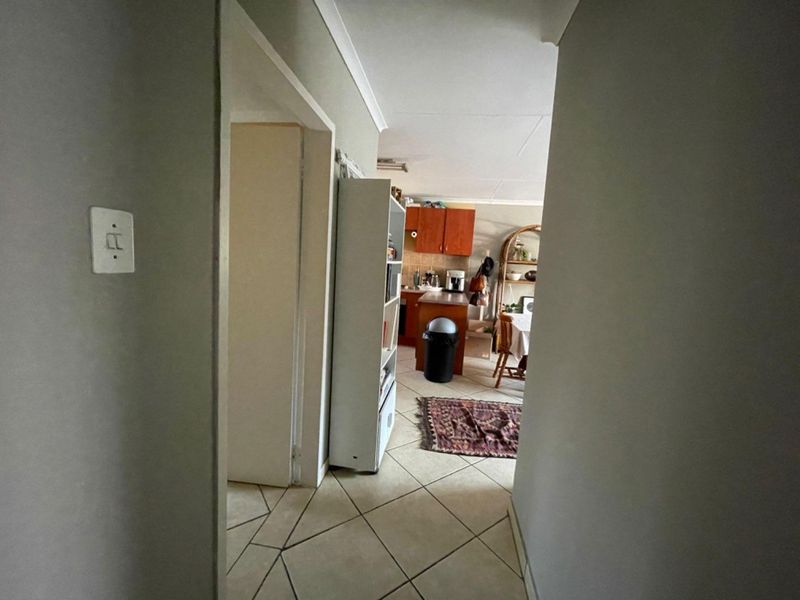 A view from a hallway into an open-plan living and kitchen area featuring tiled flooring and wooden cabinetry.