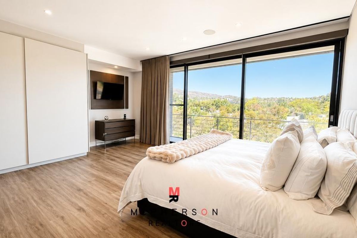 Spacious modern bedroom featuring large sliding glass doors with scenic views, built-in cabinetry, and high-quality laminate flooring.