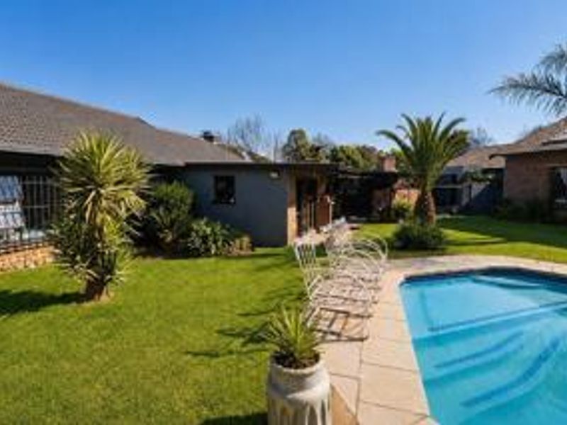 A well-maintained rear garden featuring a swimming pool with a paved surround and established lawn area.