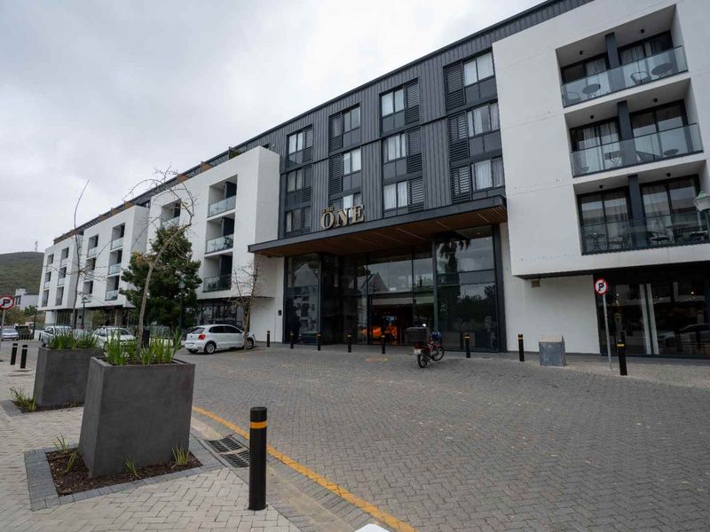 Modern apartment building exterior featuring a paved entrance, glass facade, and contemporary architectural design with private balconies.