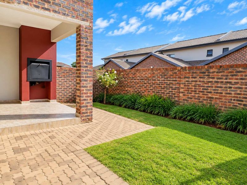 A covered patio featuring a built-in braai, overlooking a private garden with a paved area and brick boundary wall.