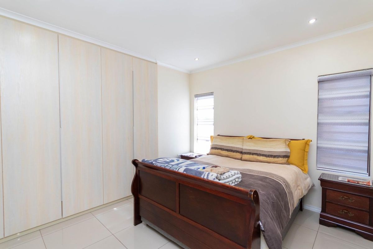 A bright bedroom featuring neutral floor tiles, recessed ceiling lighting, and built-in floor-to-ceiling wardrobes.