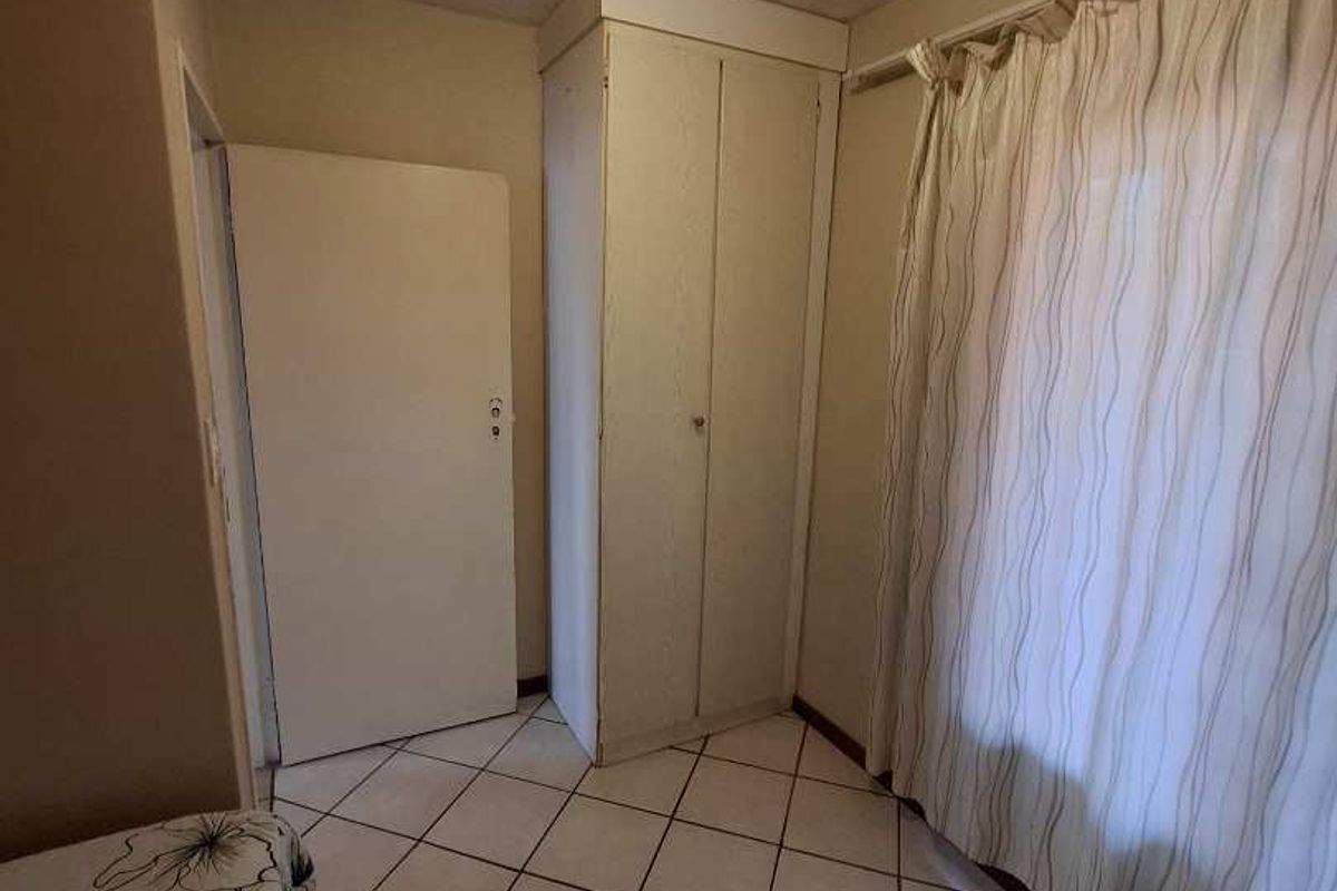 A bedroom featuring tiled flooring and a built-in cupboard, showing signs of wear on the ceiling and floor finishes.