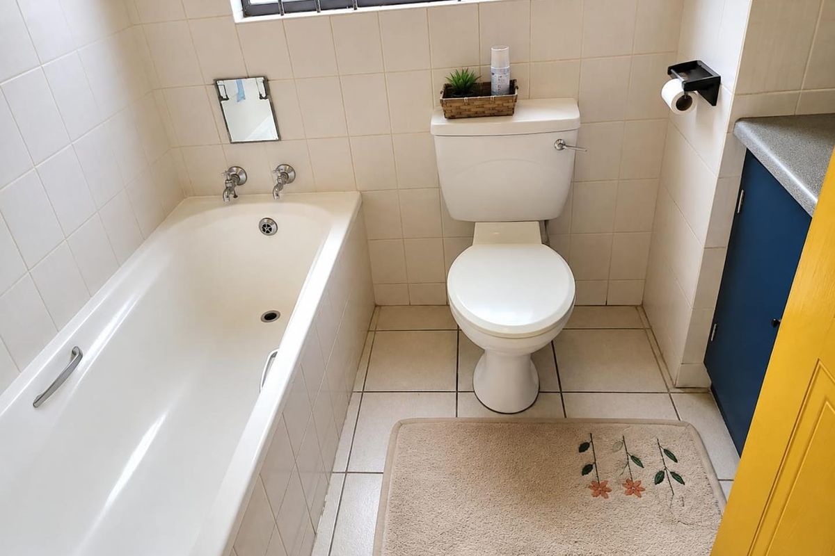 A functional bathroom featuring a standard bathtub, toilet, and vanity cabinet with tiled finishes throughout.