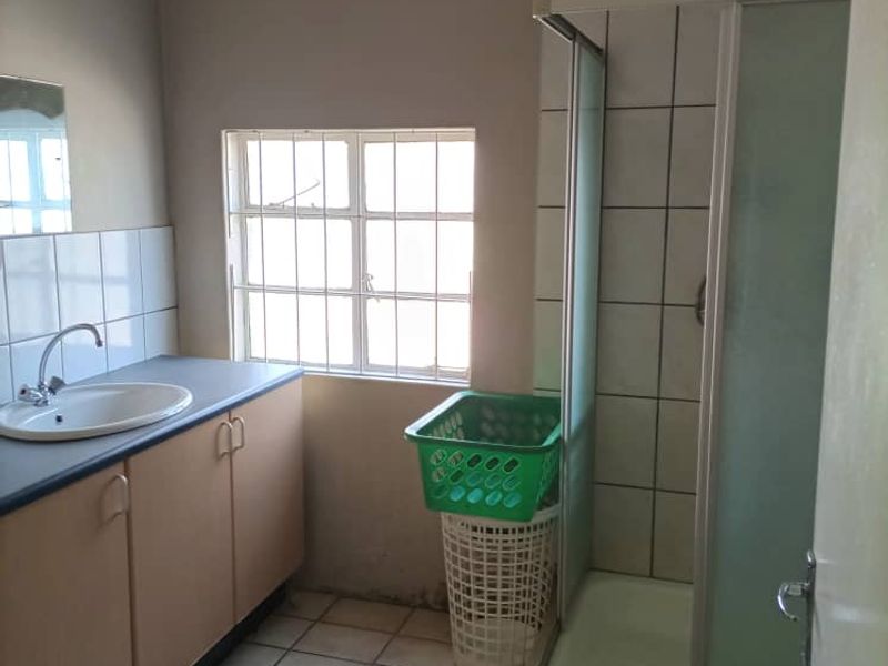 A functional bathroom featuring a shower enclosure, vanity cabinet with basin, and tiled flooring, requiring some cosmetic updates to improve its overall condition.