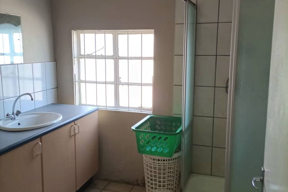 A functional bathroom featuring a shower enclosure, vanity cabinet with basin, and tiled flooring, requiring some cosmetic updates to improve its overall condition.